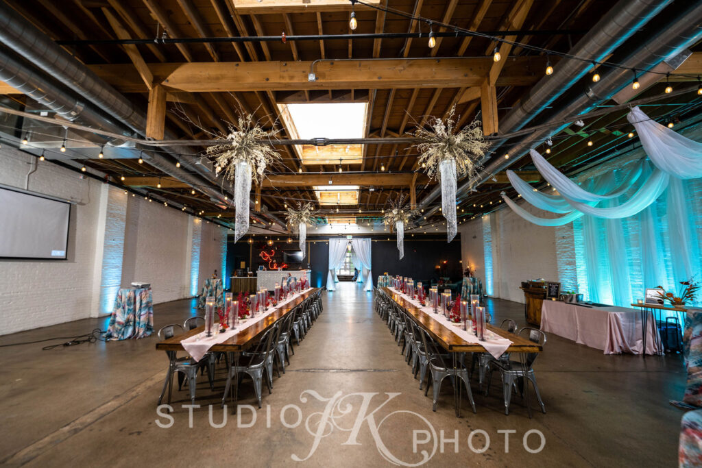 Two long tables set up for a holiday party with draping hanging from the ceiling and floral arrangements attached to the rafters.