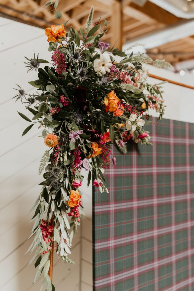 A ceremony backdrop featuring a Scottish Tartan and florals on top of a copper arch at SKYLIGHT in Denver, CO.