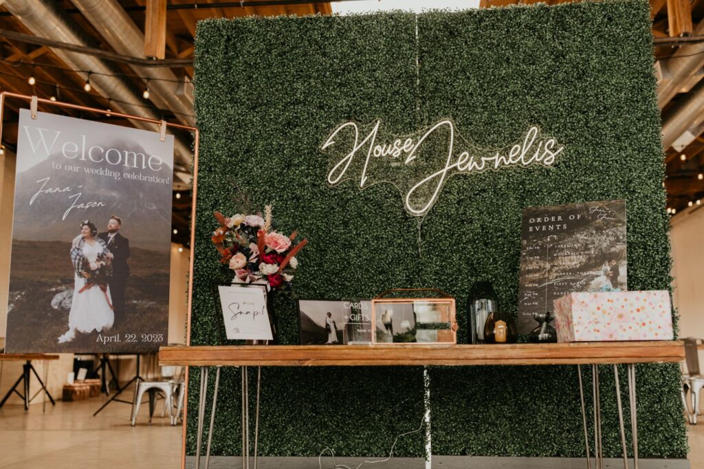 A greenery wall with a table in front of it holding a guest book and gift box at a wedding at SKYLIGHT in Denver, CO.