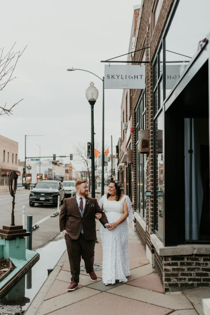 A bride and groom walking down the sidewalk in front of SKYLIGHT on their wedding day.