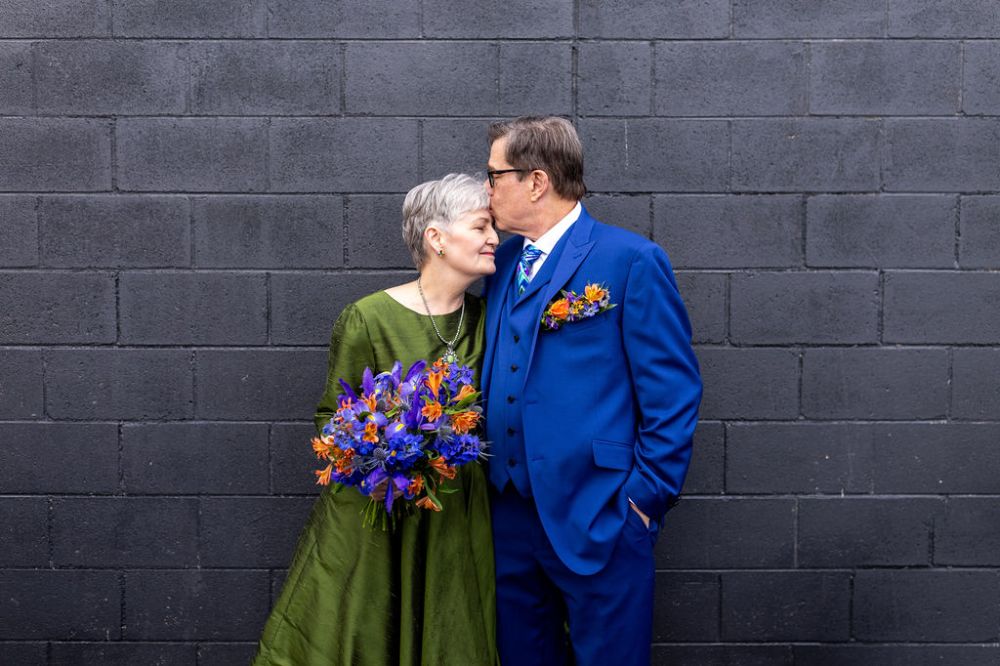 A groom in a bright blue tuxedo kisses his bride wearing a green dress