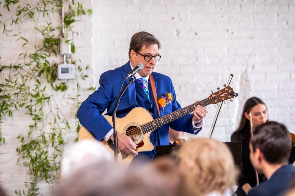 Groom in blue suit plays guitar and sings at his wedding