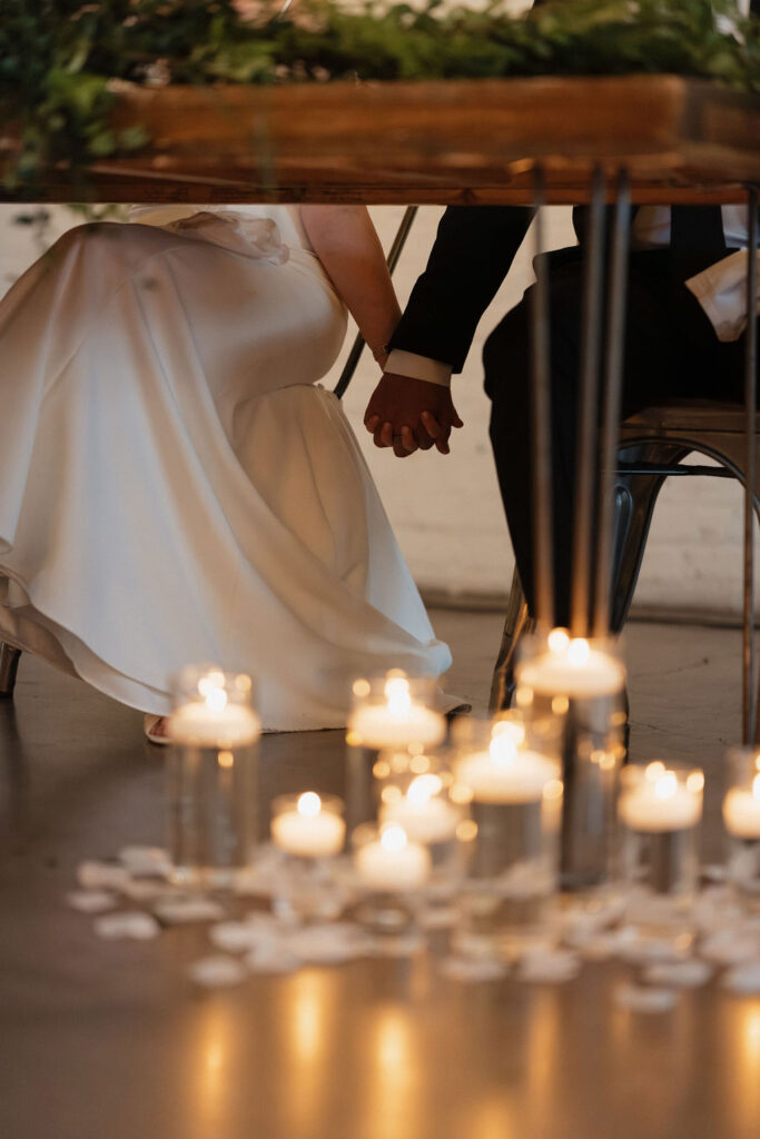 Couple holding hands underneath their sweetheart table, surrounded by candles