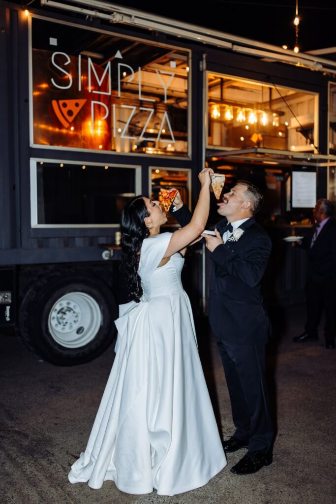 Bride and groom feeding each other pizza at their wedding