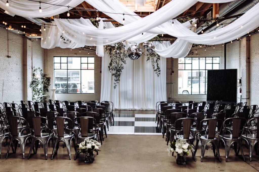 Wedding ceremony setup at SKYLIGHT in Denver, Colorado, featuring white draping, disco balls, and modern black-and-white aisle flooring.