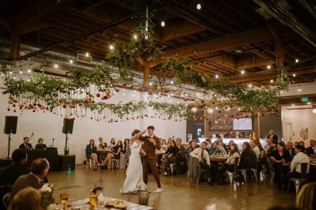 Bride and groom share a kiss at the altar during a candlelit indoor ceremony at SKYLIGHT Denver wedding venue, with guests applauding in a modern white-brick venue.