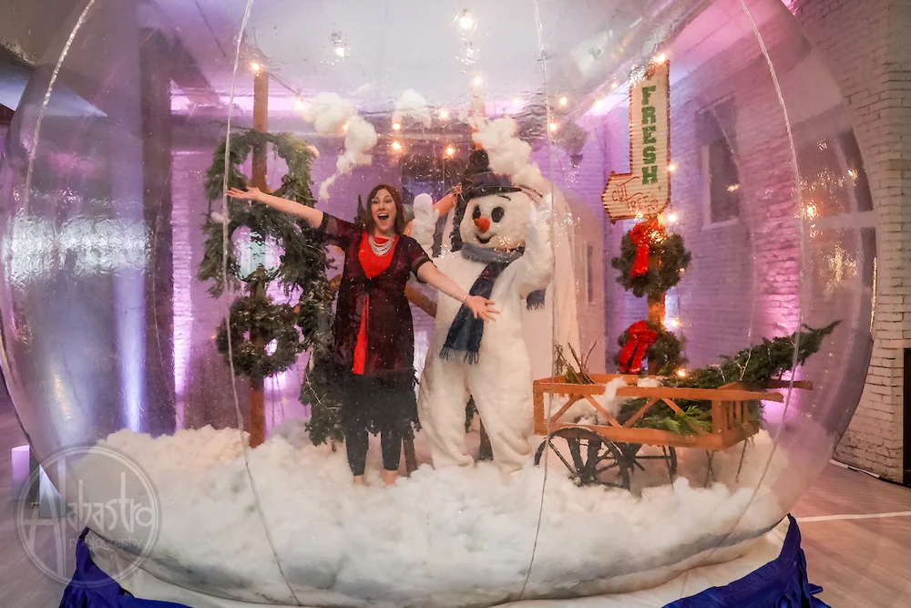 Woman standing inside of a giant snowglobe with a snowman and holiday decor at Denver office holiday party