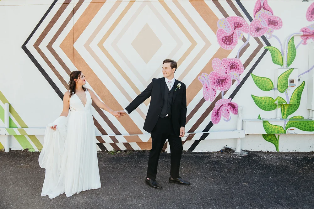 Bride and groom holding hands in front of a colorful mural in the Santa Fe Arts District of Denver