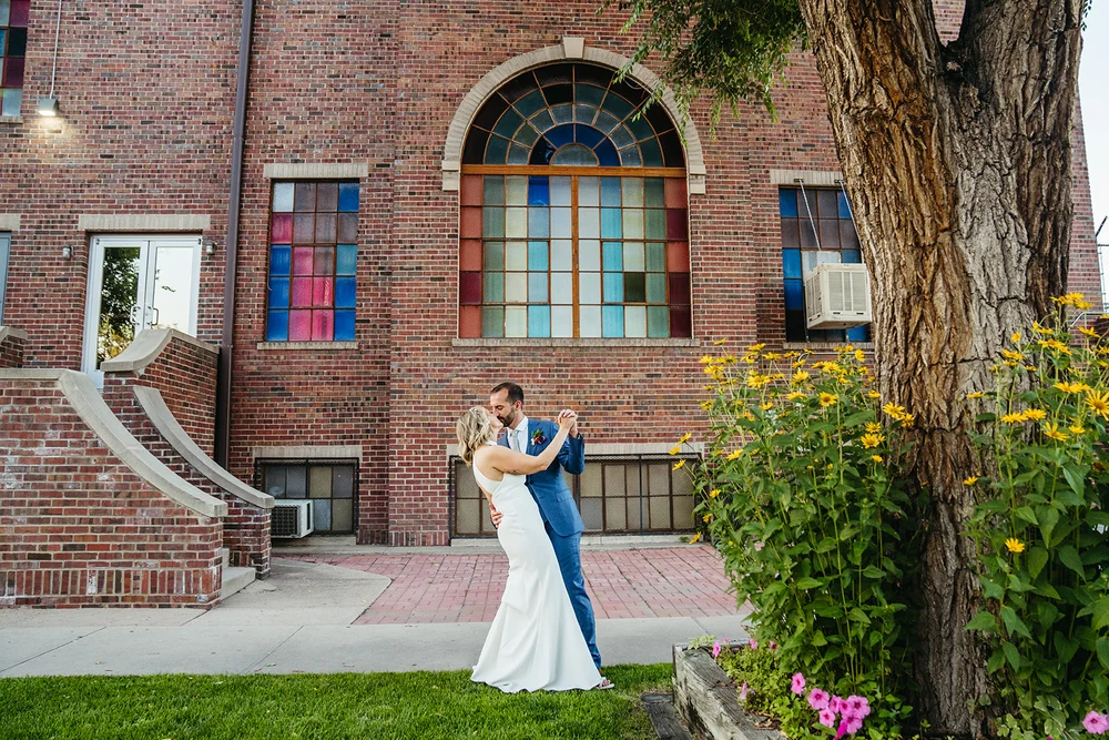 Bride and groom posing in front of a building with stained glass windows in Denver for wedding photos