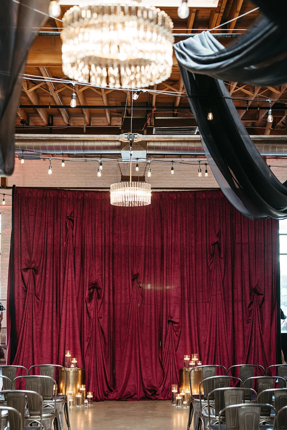 Wedding ceremony setup with a red draping backdrop and black draping hanging from the ceiling with candlelight at the altar