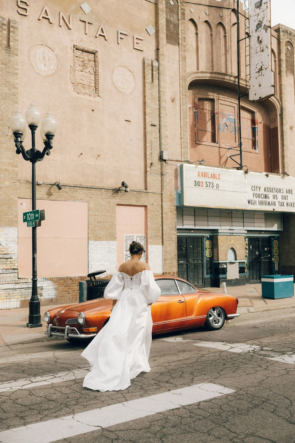 Woman posing in front of a vintage orange car outside a theater in Denver for a styled photo shoot