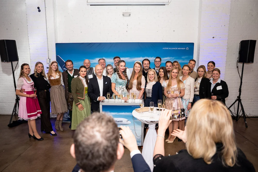 Group of guests posing in front of a travel-themed backdrop at SKYLIGHT Denver event