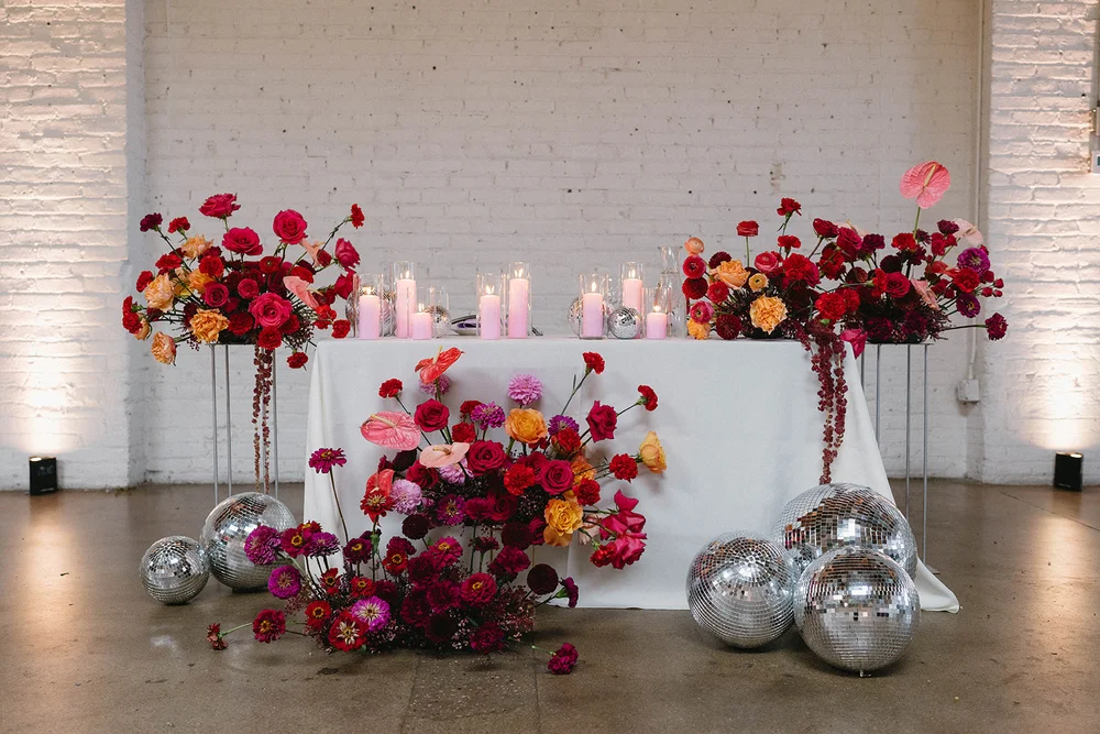Sweetheart table at SKYLIGHT with bright pink, red and orange florals, disco balls and pink candles